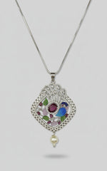 A peacock-shaped necklace pendantwith blue, green, and gold enamel accents and white faux pearl. Pendant in a silver chain is focused in this image.