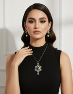 Silver polished a peacock pendant with vibrant green, blue, and gold enamel accents, along with sparkling embellishments, accompanied by matching earrings, displayed on a black mannequin necklace stand.