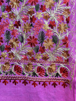 A pink base colour floral multi-colour embroidered shawl in an elegant room with curtains and furniture.
