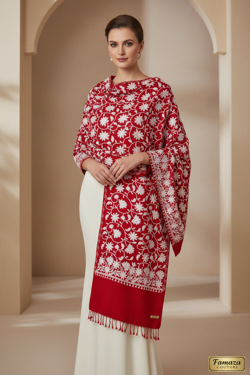 A red Kashmiri embroidered pashmina scarf with white floral patterns and tassels on the ends, displayed against a golden background.