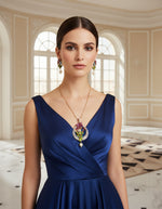 A rhodium-gold plated brass pendant with a peacock design accompanied by earrings, featuring vibrant green, blue, and gold enamel accents, as well as sparkling white and ruby pink crystal embellishments. 