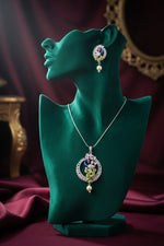A rhodium-silver plated brass pendant with a peacock design accompanied by earrings, featuring vibrant green, blue, and gold enamel accents, as well as pink AD sparkling crystal embellishments.