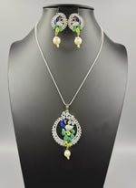 A rhodium-silver plated brass pendant with a peacock design accompanied by earrings, featuring vibrant green, blue, and gold enamel accents, as well as sparkling white AD stones embellishments.
