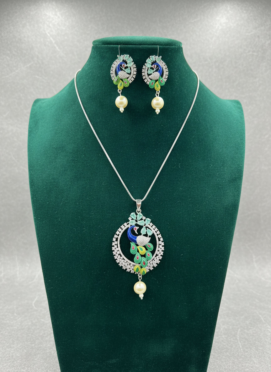 A rhodium-silver plated brass pendant with a peacock design accompanied by earrings, featuring vibrant green, blue, and gold enamel accents, as well as sparkling white and turquoise ad crystal embellishments. Party wear jewellery set. 