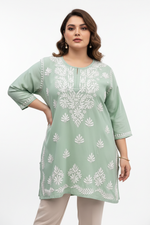 A woman modeling a sage green kurta with white floral embroidery, paired with beige trousers, against a plain white studio background.