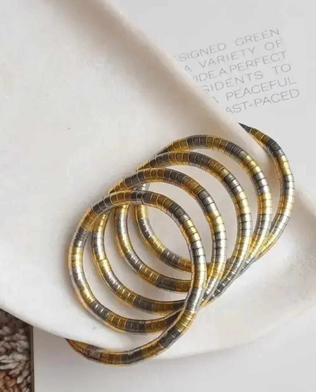 A set of gold and silver segmented hoop earrings arranged on a white ceramic dish with printed text.