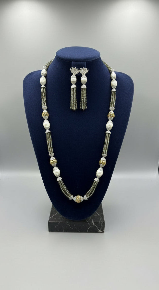 A set of jewellery featuring a long necklace with grey-coloured glass beads and metallic accents, paired with matching earrings, displayed on a mannequin bust. Party wear set. 