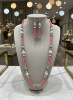 A set of jewellery featuring a long necklace with pink-coloured glass beads and metallic accents, paired with matching earrings, displayed on a mannequin bust. Party wear set. 