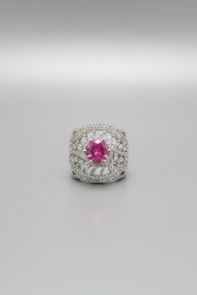 A silver-toned filigree ring with a prominent round pink gemstone, shown worn on a finger against a black background.