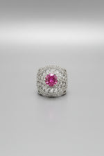 A silver-toned filigree ring with a prominent round pink gemstone, shown worn on a finger against a black background.