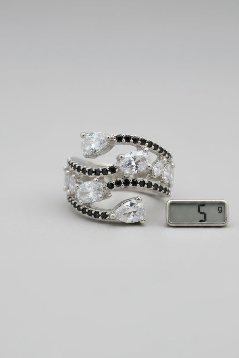 A silver-toned wrap cuff ring with marquise and oval iridescent clear stones and small dark accent stones, displayed on a black textured surface.