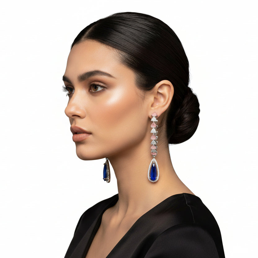 A silver finish American diamond Jhumka bali earrings with green and clear stones on a stand.