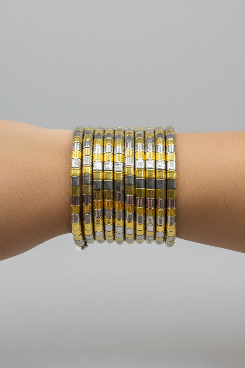 A stack of multiple bangle bracelets with alternating yellow-gold and silver metallic segments, worn on a person's wrist against a dark background.