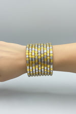 A stack of wide bangle bracelets with alternating translucent yellow and silver metallic segments, held in a hand against a black background.