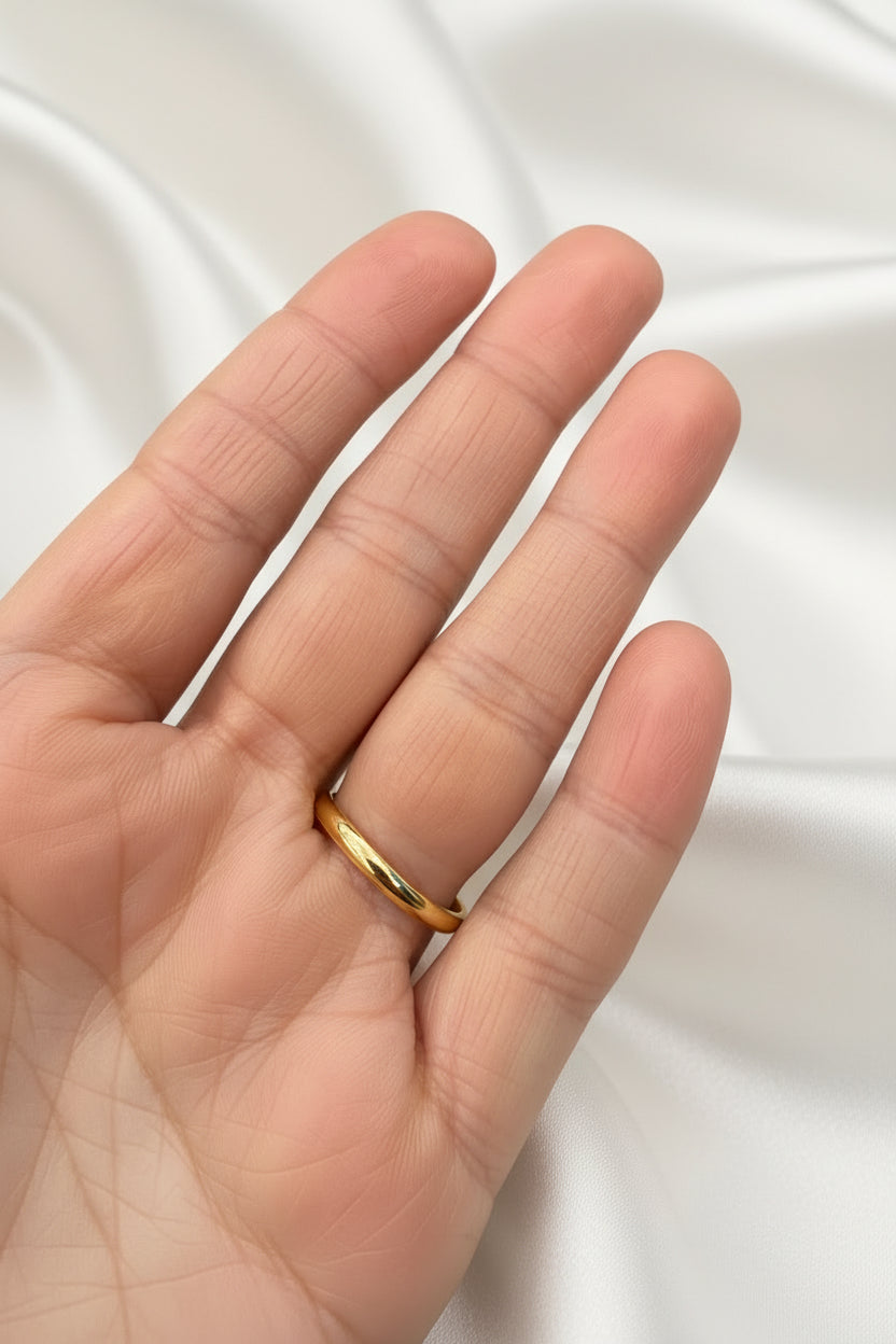 A thin, polished gold band ring worn on the ring finger of a hand, shown against a dark blue textured background.
