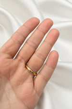A thin, polished gold band ring worn on the ring finger of a hand, shown against a dark blue textured background.