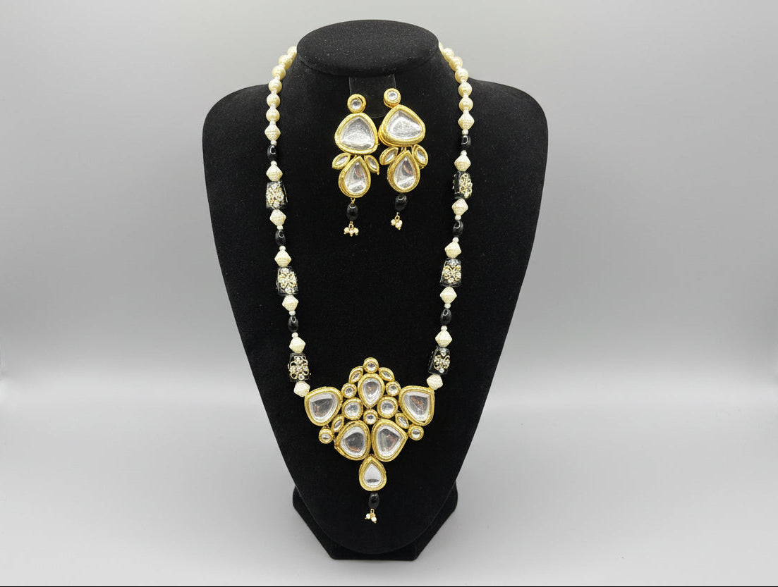 A traditional bridal kundan necklace set displayed on a mannequin, featuring black and gold colours with intricate detailing and pearl beads.