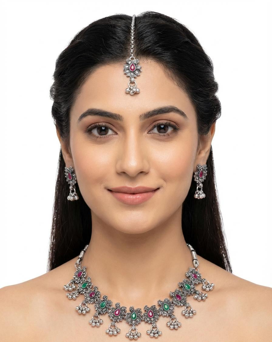 A vintage-style oxidised silver necklace with ruby and emerald floral patterns and metallic bead droplets.