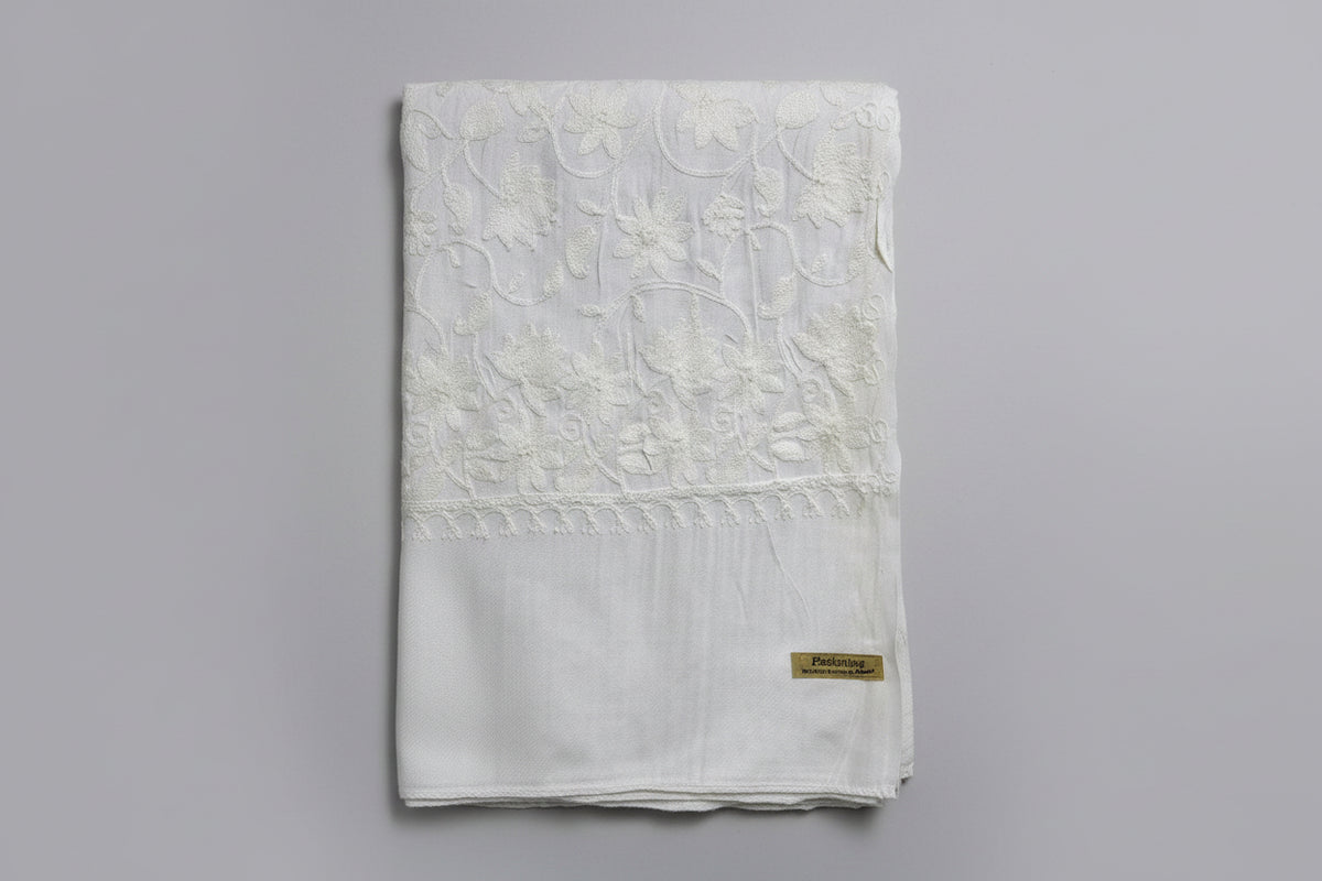 A white Kashmiri embroideredpashmina scarf with white floral patterns and tassels on the ends, displayed against a golden background.