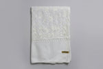 A white Kashmiri embroideredpashmina scarf with white floral patterns and tassels on the ends, displayed against a golden background.
