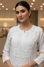 A white modal fabric dense Ghasspati embroidered Kurti is displayed in the Famaza Couture Boutique. Focus is the kurti and on it's hand embroidery for the customers to understand the pattern. 