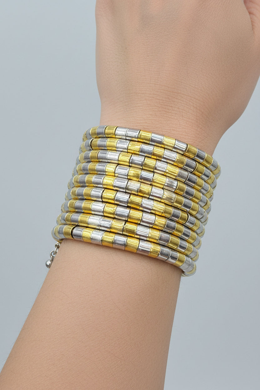 A wide cuff bracelet made of alternating yellow and silver-toned rectangular links, worn on a person's wrist against a black background.