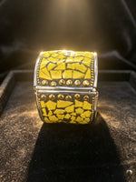 A wide silver-toned cuff ring featuring a textured yellow mosaic inlay, displayed on a black velvet jewellery.