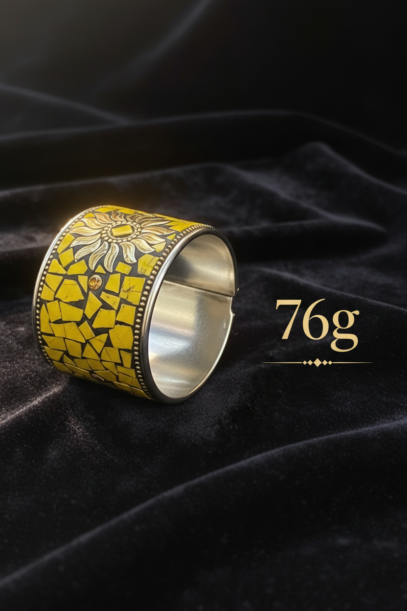 A wide silver-toned cuff ring with a yellow mosaic-style enamel pattern and a sunflower motif, displayed on a black velvet fabric background with the text '76g' beside it.
