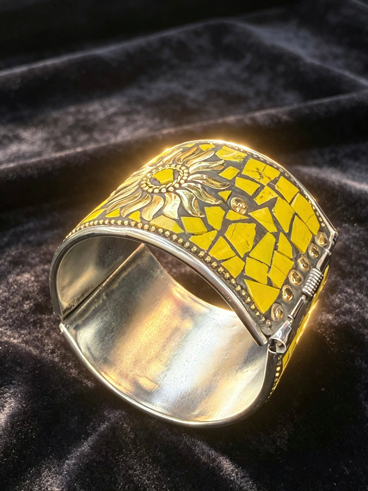 A wide silver cuff bracelet featuring a yellow mosaic tile pattern and a sunflower design, displayed on a dark velvet background.