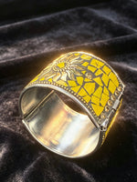 A wide silver cuff bracelet featuring a yellow mosaic tile pattern and a sunflower design, displayed on a dark velvet background.