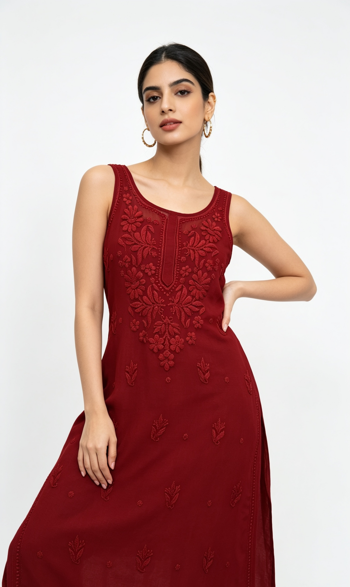 A woman modelling a sleeveless, floor-length maroon red dress with intricate floral embroidery on the bodice and scattered embroidered motifs on the skirt, set against a plain white studio background.