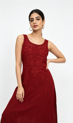 A woman modelling a sleeveless, floor-length maroon red dress with intricate floral embroidery on the bodice and scattered embroidered motifs on the skirt, set against a plain white studio background.