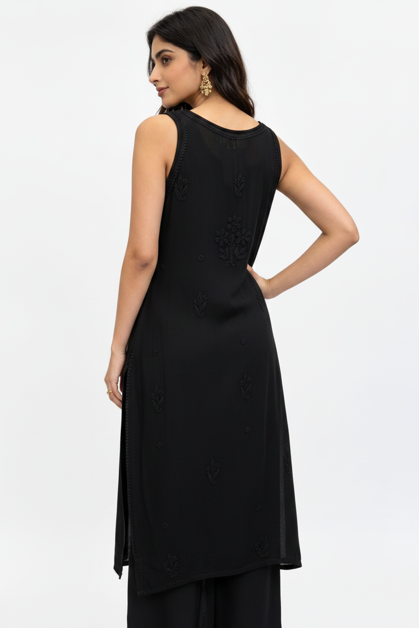A woman modeling a sleeveless black kurta from the back, featuring subtle embroidered details, paired with black trousers against a plain white studio background.