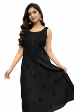 A woman modeling a sleeveless black maxi dress with tonal floral embroidery and a round neckline, shown against a plain white background.