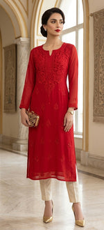 A woman models a red embroidered kurta with three-quarter sleeves, paired with cream pants and gold heels, holding a small patterned clutch in an elegant indoor setting.