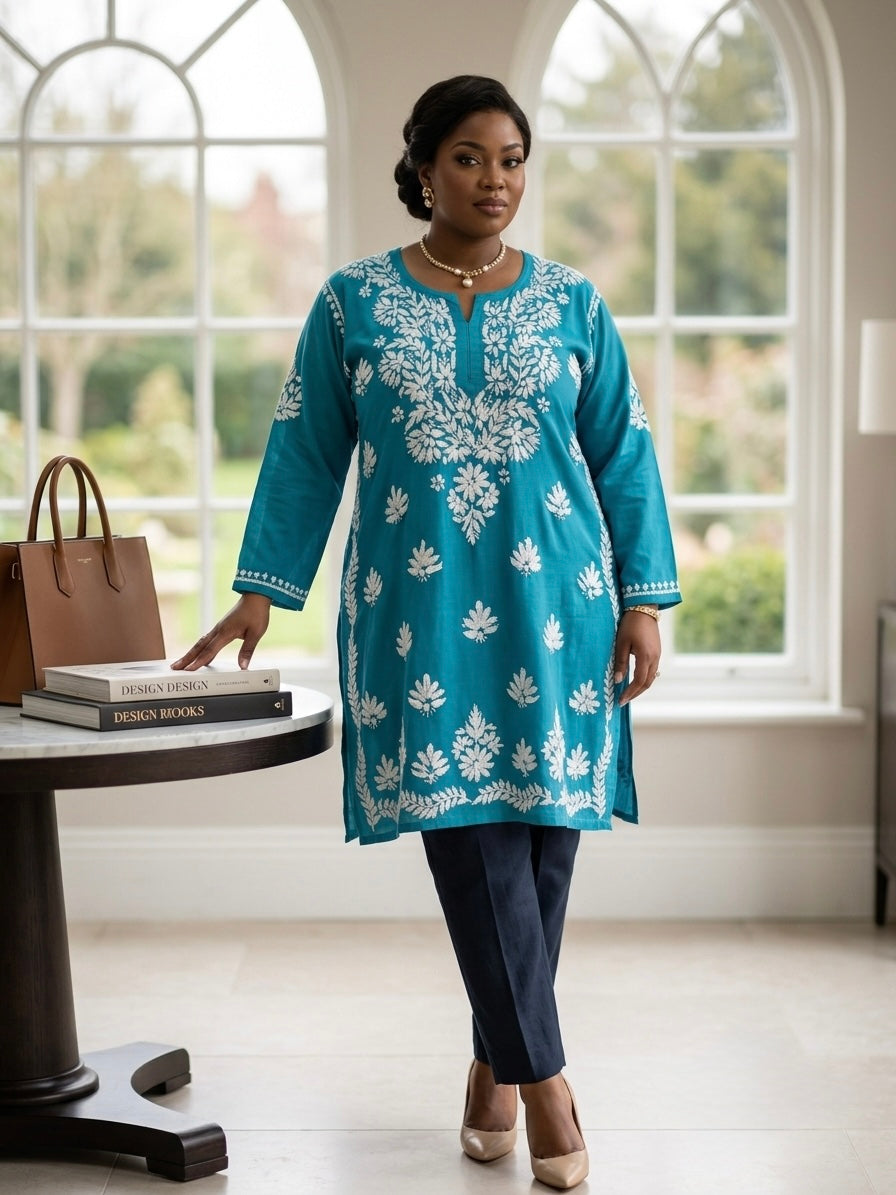 A woman models a teal blue kurta with white floral embroidery, paired with navy blue trousers and beige heels, standing in a bright room with large arched windows.