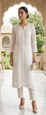 A woman models a traditional white Indian kurta set with matching trousers in an outdoor architectural setting with arches.