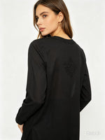 A woman shown from the back wearing a black long-sleeve tunic top with a subtle tonal embroidered motif on the upper back, photographed against a clean white studio background.