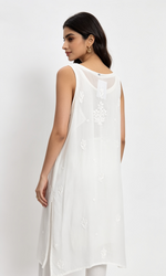 A woman shown from the back wearing a sleeveless white kurta with delicate floral embroidery and a sheer neckline, paired with white trousers, against a plain light background.