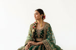 A woman wearing long brass tassel earrings featuring emerald green circular studs and golden ghungroo clusters.