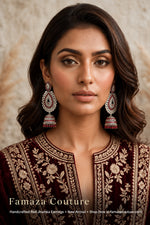 A woman wearing ornate red and silver jhumka earrings with a deep maroon embroidered top, posed against a textured beige background. Text overlay at the bottom reads 'Famaza Couture'.