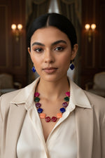 A young woman modeling the Royal Blue variant of the Facet Rhombus Necklace. The image highlights the bright magenta and deep green diamond beads against her skin, paired with matching royal blue rhombus-cut earrings for a high-contrast, trendy jewelry look.