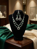 American Diamond necklace , earrings and maag tikka with bottle green centre stones displayed on a velvet stand with ornate background