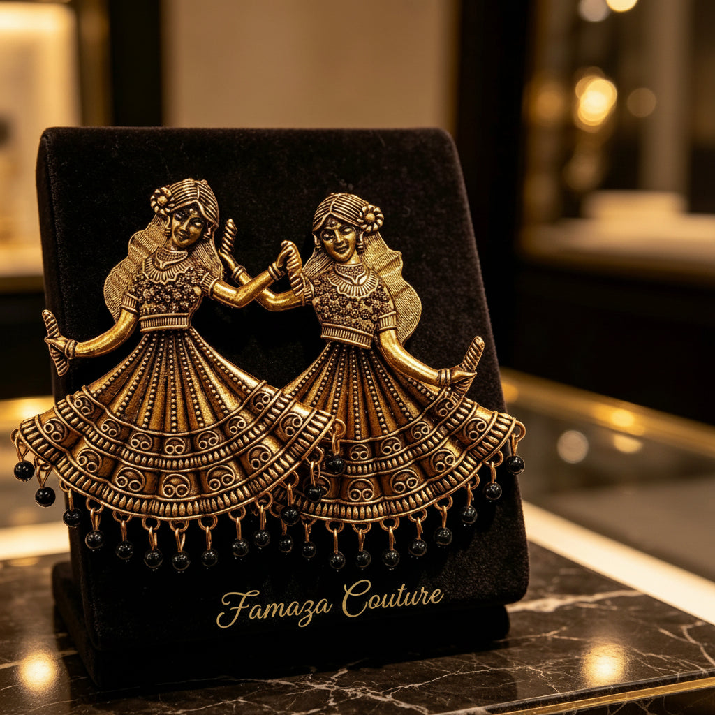 An ornate gold-toned jewellery piece depicting two dancing figures in detailed traditional attire, displayed on a black velvet stand over a polished dark marble surface.