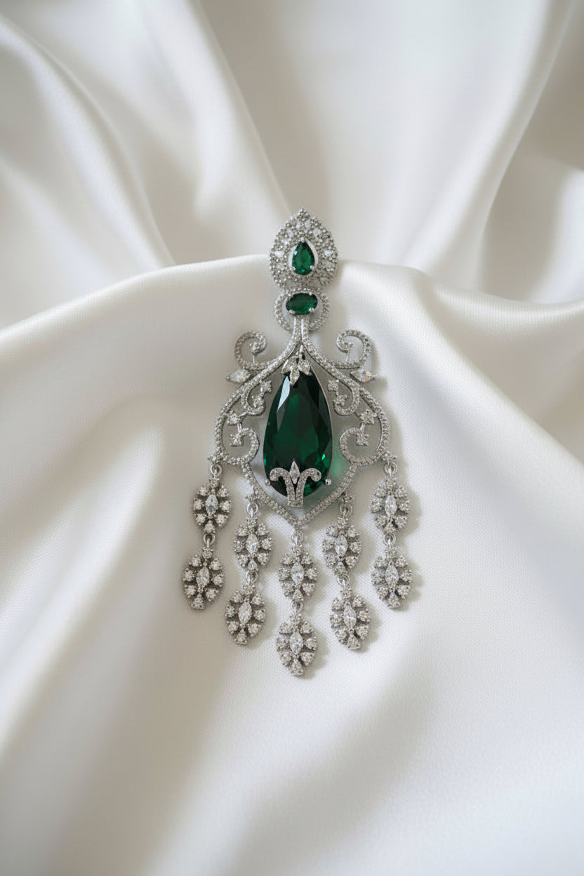 An ornate silver-toned American diamond earring featuring a large dark green teardrop-shaped gemstone, two smaller green pear-shaped stones, and multiple clear pavé-set crystals forming leaf and scroll motifs, displayed.