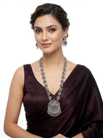 A model wearing a long-line vintage oxidized silver necklace with an intricate floral lattice design and matching drop earrings, featuring ruby and emerald-toned stone accents and white pearl droplets.