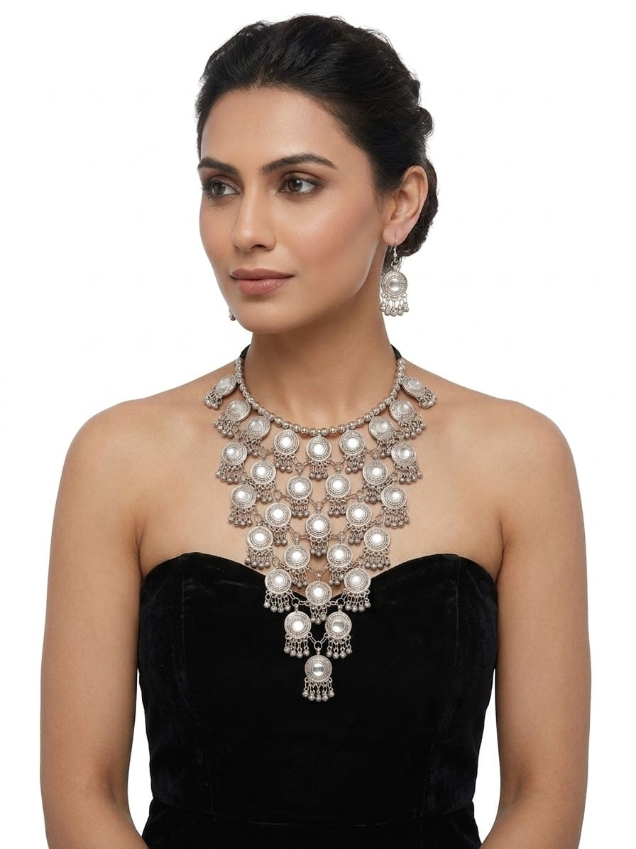 Oxidized silver tiered Y-shaped statement necklace set with mirror accents and matching jhumka dangle earrings — worn with black strapless outfit, South Asian bridal & party jewelry.