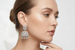 A close-up of a woman wearing a pair of silver-toned, diamond-encrusted traditional Indian jhumka earrings and a matching double-strand necklace.