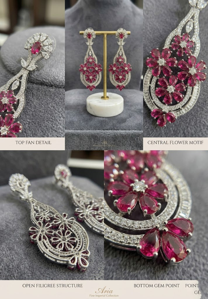 Aria Imperial pink ruby and diamond chandelier drop earrings displayed elegantly on a gold T-bar stand with a white marble base against a grey velvet background.