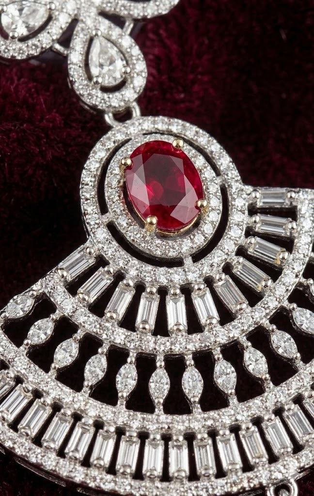 Close-up view of the Aria luxury earring featuring a vibrant oval red stone centerpiece surrounded by precisely set rectangular baguette and round cz diamonds.